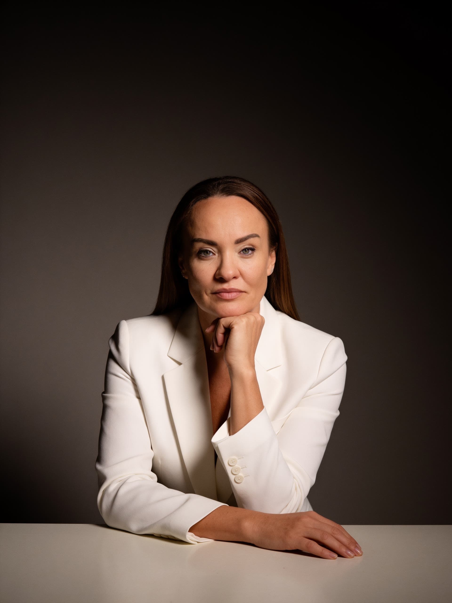 Portret editorial — Oana Voda în sacou alb, pe fundal întunecat, într-un moment de concentrare